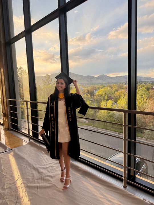 Sukriti in graduation robes and a DASSA stole in front of the Boulder foothills