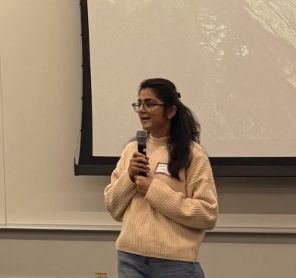 Sukriti speaking into a microphone as Chair of DaSSA